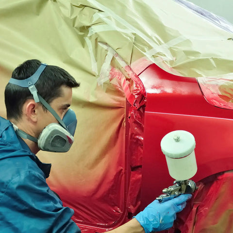 Person using spray gun to paint a car with a red finish while wearing safety gear and blue gloves.