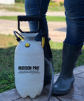 1.5 Gallon Bleach Sprayer With Durable Viton Seals For Home And Yard Cleaning, held by person in boots on a lawn