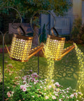 Two Pack Solar Watering Can Garden Lights, Hanging Waterproof Lanterns casting cascading glow over flowers at night