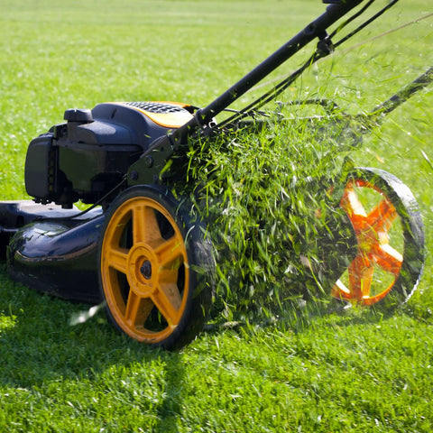Side view of a black and orange gas-powered lawn mower with yellow wheels cutting grass.