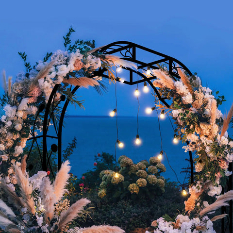 Tall Black Garden Arch Trellis 8.2 Ft High 6.2 Ft Wide Outdoor Arbor For Climbing Plants Roses And Vines Built To Last Perfect Lawn Wedding Archway Durable Weatherproof Construction decorated with flowers and lights at night by the sea