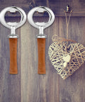 Two Cunhill metal bottle openers with brown wooden handles on a wooden backdrop; wicker heart decor.