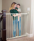 Tall Easy Swing and Lock Baby Gate Series 2 mounted at the top of stairs with a woman holding a child nearby
