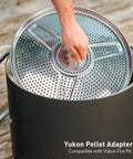 Hand placing Yukon Pellet Adapter For Outdoor Fire Pit, Dual Fuel Conversion Accessory into a steel pit, 23.7 inch diameter.