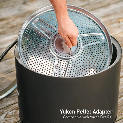 Hand placing Yukon Pellet Adapter For Outdoor Fire Pit, Dual Fuel Conversion Accessory into a steel pit, 23.7 inch diameter.
