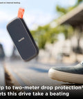 1TB Portable SSD With Up To 800 MB Per Second Read Speeds, USB C And USB 3.2 Gen 2, with rugged drop proof design next to shoe.