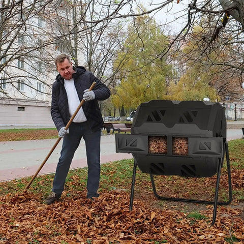Dual Chamber Tumble Composter 43 Gallon Rotating Bin With 360 Degree Tumbler For Fast Easy Garden Waste Recycling BPA Free Black Outdoor Compost System next to a man raking leaves in a park.