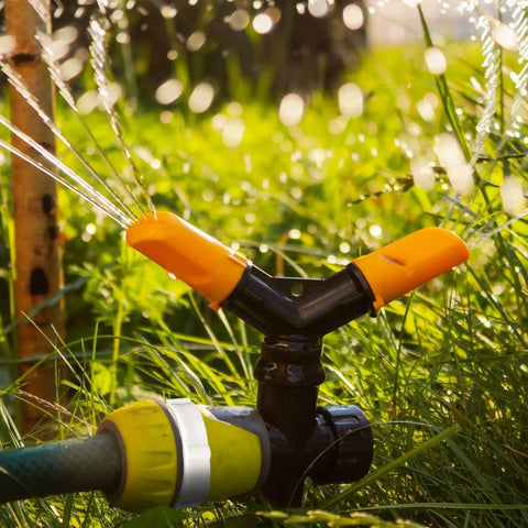 Garden sprinkler system with black and orange PVC fittings irrigating grass outdoors