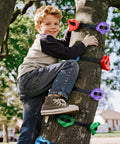 Child using Ninja Tree Climbing Holds Set For Kids And Grownups on tree, showing colorful resin rocks and straps outdoors.