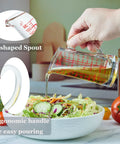 Hand pouring liquid from Glass Measuring Cup 5 Oz 150 Ml Shot Glass With V Spout And Insulated Handle onto salad