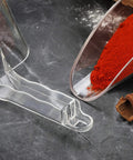 Commercial Grade Polycarbonate Ice Scoop 24 Ounce Clear Utility Scoop For Ice Flour And Sugar In Busy Kitchens Real Kitchen Workhorse Break Resistant With Beveled Front Edge For Easy Scooping And Spill Prevention next to a scoop of red spice on a countertop.