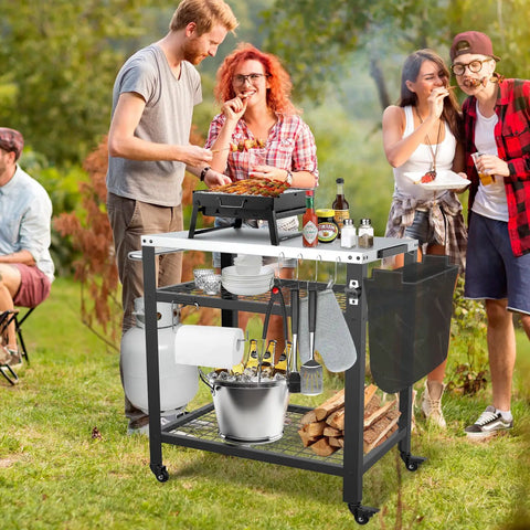 Stainless Steel Pizza Oven Table For Ooni And Other Grills Heavy Duty Outdoor Grill Cart With Wheels And Handle 32 By 24 Inch Three Shelf Food Prep Cart For Griddle Movable Outdoor Pizza Cart shown in use at an outdoor gathering.