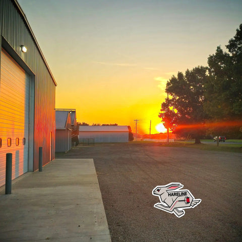 Sunset view of a rural road next to a metal warehouse with Hareline logo visible on the ground.