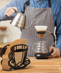 Durable Coffee Filter Holder And Paper Storage Rack With Cup Shaped Stand For Fan Shaped T Shaped And Square Paper Filters Must Have For Home Kitchen Restaurant Picnic Or Wedding Accessory on a kitchen counter with a barista brewing coffee in the background.