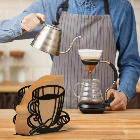 Durable Coffee Filter Holder And Paper Storage Rack With Cup Shaped Stand For Fan Shaped T Shaped And Square Paper Filters Must Have For Home Kitchen Restaurant Picnic Or Wedding Accessory on a kitchen counter with a barista brewing coffee in the background.