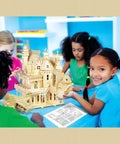 Children building a wooden castle model in a classroom setting with instruction booklet visible.