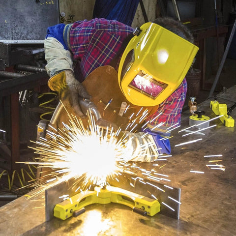 Magswitch Pivot Angle 200 welding magnet, yellow, front view clamped to metal workpiece during welding with sparks