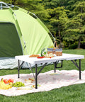 34 Inch Square Folding Card Table Portable Utility Dining Table Heavy Duty HDPE White Plastic Foldable With Carrying Handle Indoor Outdoor For Picnic Camping Party set up outside a green tent with picnic items on top.