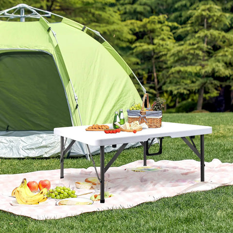 34 Inch Square Folding Card Table Portable Utility Dining Table Heavy Duty HDPE White Plastic Foldable With Carrying Handle Indoor Outdoor For Picnic Camping Party set up outside a green tent with picnic items on top.