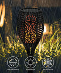 Solar Flame Torch Lights 4 Pack with flickering flame waterproof solar pathway lights glowing in rain among garden grass.