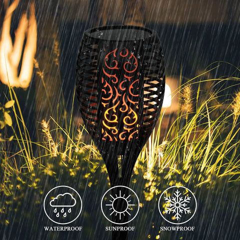 Solar Flame Torch Lights 4 Pack with flickering flame waterproof solar pathway lights glowing in rain among garden grass.