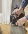 A close-up of a person using the Rock Solid Heavy Lifter 20V Compact Circular Saw Kit for flush trimming near a baseboard.