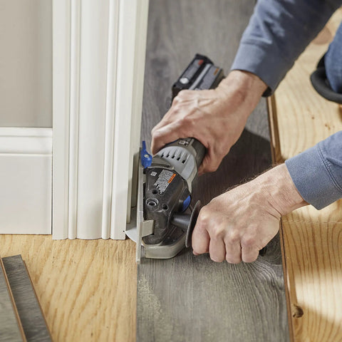 A close-up of a person using the Rock Solid Heavy Lifter 20V Compact Circular Saw Kit for flush trimming near a baseboard.