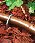 Installed view of Heavy Duty Galvanized 6 Inch Workhorse Ground Stake Set For Half Inch Drip Irrigation Tubing 10 Pack Keeps Tubing In Place All Weather Corrosion Resistant 12 Gauge Steel securing brown tubing in garden mulch.