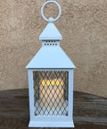 White rustic vintage lantern with LED candle, part of the 12 Piece 10 Inch Decorative Lantern Set With Flameless LED Candles And 5 Hour Timer For Indoor Outdoor Use White Rustic Vintage Look Weather Resistant Garden Patio Weddings Includes Bonus String Lights, on wooden table.