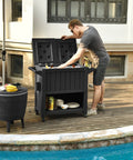 Man using the 85 Quart Wheel Cart Cooler For Patio And Pool Deck Party Outdoor Beverage Station with open lid by a pool.
