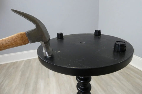 Installing 16 Pack Self Leveling Table Glides With Quarter Inch Threaded Stem on a round black table using a hammer