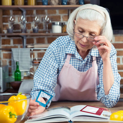 Senior woman using 2 Pack Large Full Page Magnifying Sheet With 3X Magnification And 3 Fresnel Lens Bookmark Magnifiers in kitchen