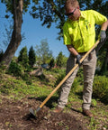 Worker using Heavy Duty Steel Rake Hoe With Wood Handle And Five Wide Tines For Quick Cultivation in a garden setting