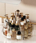 Real Deal Slick Spin 360 Round Rotating Makeup Organizer Clear Acrylic Lazy Susan displaying skincare, perfumes, and brushes on vanity.