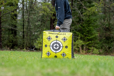 Person carrying Beast 24 Inch Dual Sided Archery Target For 475 FPS Compound Bows And Crossbows in a field.