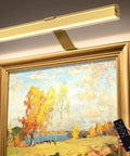 Dreamy Insert Picture Light Offering Straightforward Zero Drill Mounting And Smooth Magnetic Attachment For Hassle Free Wall Frame Illumination That Is An Absolute Game Changer. Gold magnetic picture light above framed artwork, remote in hand.