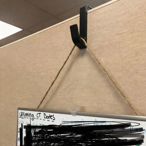 4 Pack Adjustable Cubicle Hooks For 1.8 To 3.5 Inch Panels And Walls, Plastic Coat Hooks For Laptops, Bags, Cases, And Coats, Sturdy Hangers With Easy Install, Style 1 Black clipped to cubicle wall holding a board.
