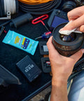 Close-up of hands wiping a camera lens with Invisible Glass lens cleaning wipes; blue 16-count package visible.