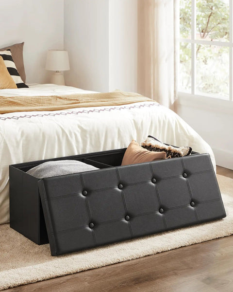 Mazie Collection 43 Inch Folding Storage Ottoman Bench With Hidden Storage Foot Rest Stool Supports Up To 660 Lb No Fuss Easy Foldaway Design For Living Room Black Synthetic Leather placed in bedroom with open lid showing storage space.