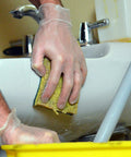 Person using Top Shelf Clear Vinyl Disposable Gloves straight up reliable 3 mil thickness for cleaning a sink with a sponge.
