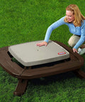 Fold N Store Picnic Table With Market Umbrella, Brown Wood Grain Finish, compact outdoor table shown folded on green grass