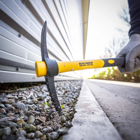 Micro Pick Mattock with Fiberglass Handle used to break ground next to a building, showcasing soft grip and corrosion resistance
