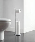 Free Standing Toilet Paper Holder With Reserve Space For Jumbo Rolls, Chrome Finish, next to toilet in minimalistic bathroom.