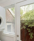 White blinds installed using 2 Inch White Low Profile Box Mount Blind Brackets Bundle, window with a view of backyard greenery.