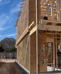 Wood framing structure during construction phase with partially built second story, showcasing support beams and blue sky in background.