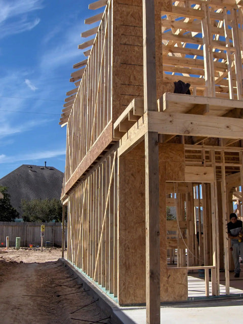 Wood framing structure during construction phase with partially built second story, showcasing support beams and blue sky in background.