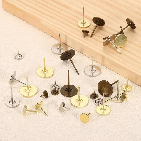 Gold Flat Head Upholstery Thumb Tacks 100 Count Top Shelf Decorative Push Nails scattered on fabric and wood, showcasing various sizes.