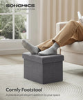 Person using Mazie Folding Storage Ottoman Foot Rest Stool With Quick Foldaway Design in dark gray as footrest in living room.