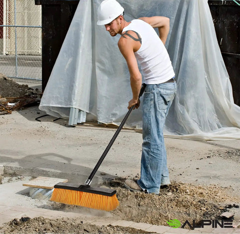 Real Deal Heavy Duty Push Broom With Long Handle Made To Crush Daily Grime On Smooth Floors Sweeps Sand Mud Leaves And Water Easy Without Breaking A Sweat In Bright Yellow 18 Inches Wide being used on construction site by worker.