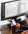 Person using a smartphone and computer on a desk, running data recovery software for Bootable USB Repair Kit For Windows PCs.